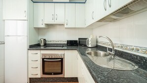 Una cocina con armarios blancos, horno doble, microondas, hervidor y un lavabo.