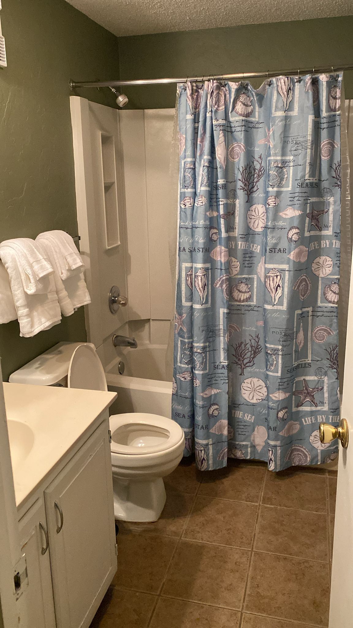 Un baño con inodoro, lavamanos y cortina de ducha con motivos marinos.