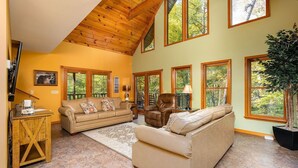 A spacious living room with a high ceiling, large windows, and a cozy seating area.