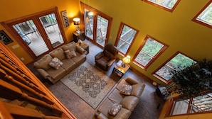 A spacious living area with a large sofa, a smaller sofa, and a coffee table. There are multiple windows providing natural light and views of the outdoors.