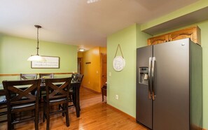 A dining area with a wooden table and chairs, a refrigerator, and a wall-mounted light fixture. - North Ridge Place - Fireplace, hot tub, and games! (Sevierville)