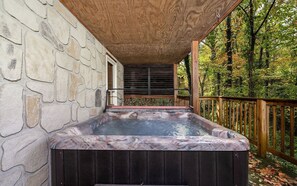 A hot tub on a wooden deck with stone walls, surrounded by trees. - North Ridge Place - Fireplace, hot tub, and games! (Sevierville)