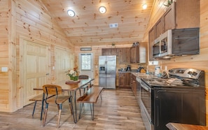 L’intérieur d’une cabane en bois comprend une table à manger, des chaises, un réfrigérateur, une cuisinière et des armoires en bois.
