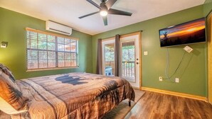 A bedroom with a bed, a ceiling fan, a window, and a TV on the wall. - Hidden Hollow Lodge - Movie Nights, Game Fun, Fireside Stories & Hot Tub Soaks (Sevierville)