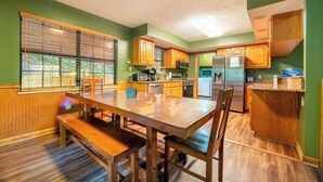 A kitchen with wooden cabinets, a dining table with chairs, and a refrigerator. - Hidden Hollow Lodge - Movie Nights, Game Fun, Fireside Stories & Hot Tub Soaks (Sevierville)