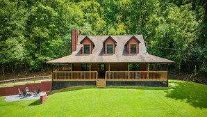 A lodge with a covered porch, a fireplace, and a deck with outdoor seating. - Hidden Hollow Lodge - Movie Nights, Game Fun, Fireside Stories & Hot Tub Soaks (Sevierville)
