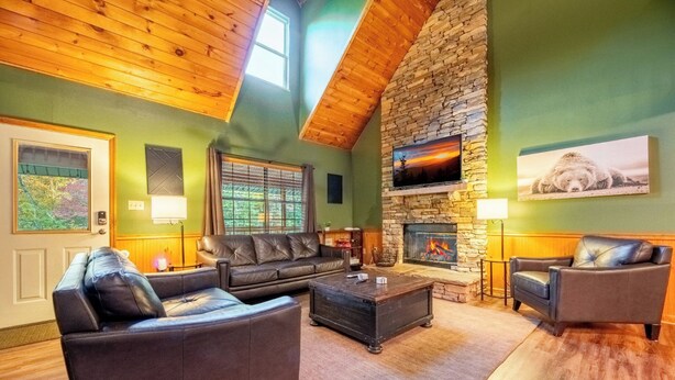 A cozy living room with a stone fireplace, leather sofas, and a wooden ceiling. - Hidden Hollow Lodge - Movie Nights, Game Fun, Fireside Stories & Hot Tub Soaks (Sevierville)