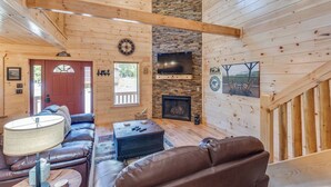 L’intérieur chaleureux d’un chalet avec une cheminée, des murs en bois, un canapé en cuir et une grande fenêtre.