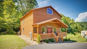 Une cabane en bois avec une véranda, une porte rouge et des fondations en pierre.