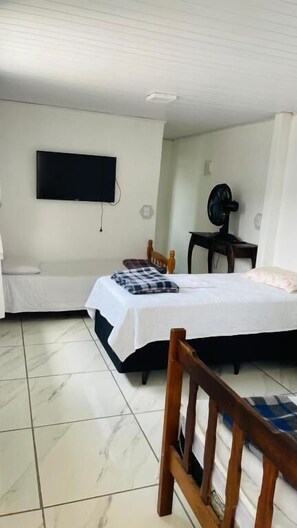 A bedroom with a bed, a television mounted on the wall, a fan, and a small table. - Pousada Don Ruan (Ponta Grossa)
