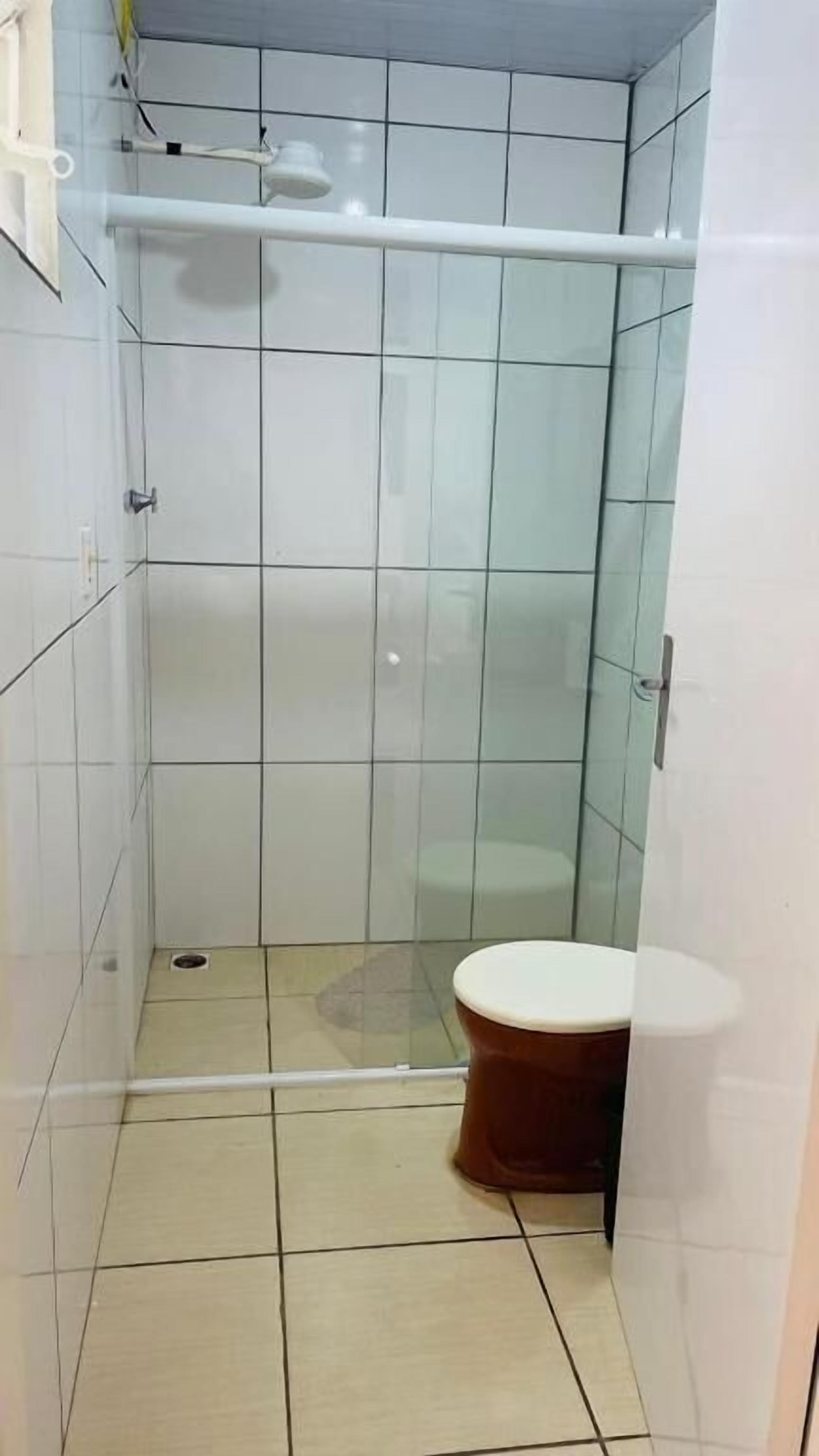 A small, tiled bathroom with a glass shower enclosure, a toilet, and a visible drain.