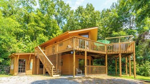 Une cabane en bois dotée d’une terrasse et d’un escalier, entourée d’arbres.