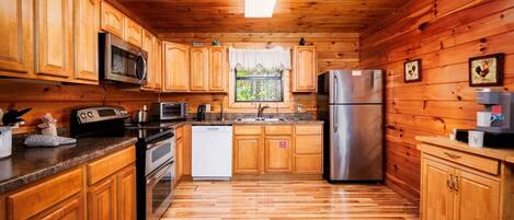 Una cocina tipo cabaña de madera con microondas, estufa, refrigerador y cafetera.