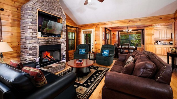 Un interior de cabaña acogedor, con chimenea de piedra, muebles de cuero y un comedor.