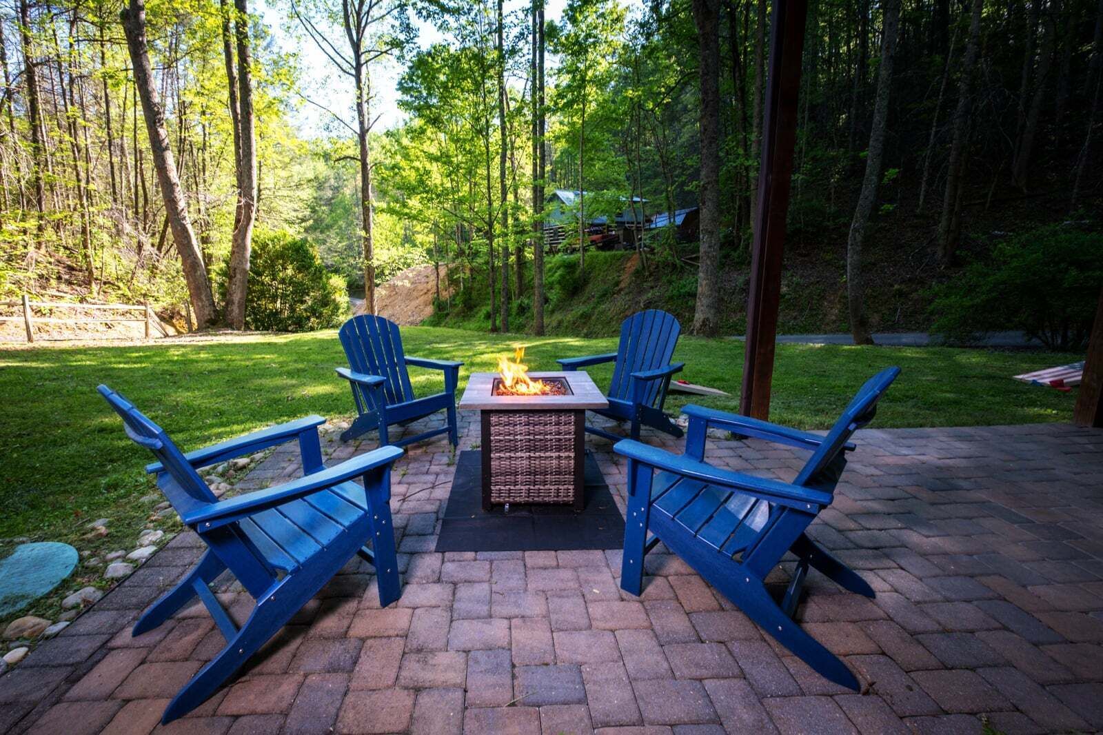 Un patio con cuatro sillas Adirondack azules, un hogar cuadrado y un piso de ladrillo.