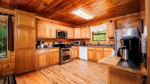 Cocina de cabaña de madera con microondas, estufa, lavavajillas y cafetera.