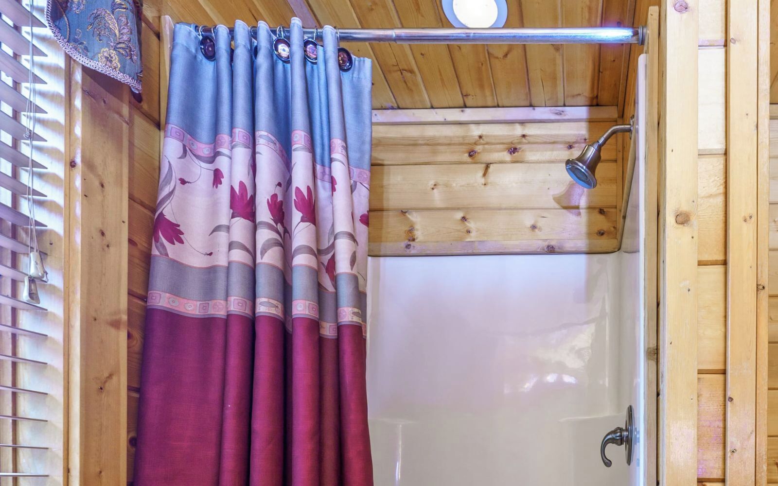 Ein Badezimmer einer Holzhütte mit Dusche, Holzboden und Vorhang mit Blumenmuster.