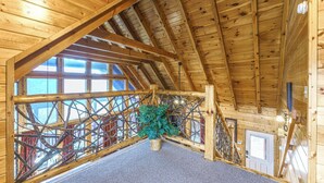 Une pièce mansardée en bois, avec un plafond en pente, une grande fenêtre et un escalier menant à l’étage supérieur.
