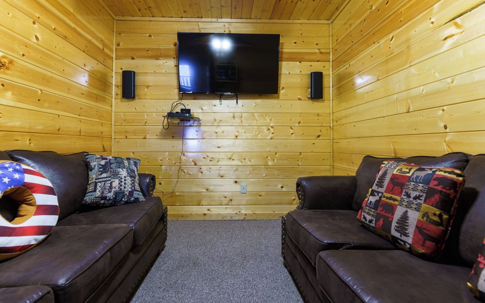 A cozy room with two leather sofas, a television mounted on the wall, and a small speaker.