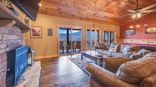 A cozy living room with a fireplace, a pool table, and a balcony with a scenic mountain view.