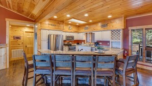 A wooden cabin interior with a kitchen featuring a central island, bar stools, and a dining table.