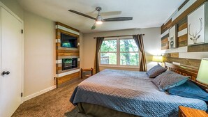Una camera da letto con un letto, una ventola a soffitto, una TV montata su una parete in legno, una finestra con tende e una testiera in legno.