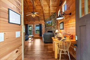 A wooden cabin interior with a dining area, a sofa, a fireplace, and a ceiling fan.
