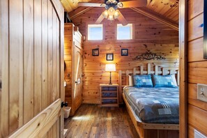 A cozy wooden cabin bedroom with a bed, nightstand, and ceiling fan. - Mountain views and a cozy hot tub! - Always (Gatlinburg)