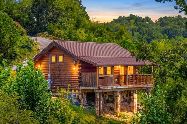 A log cabin with a balcony, surrounded by dense forest.