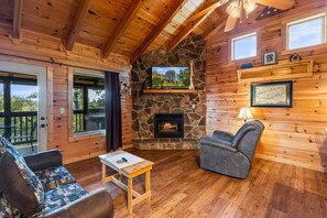 L’intérieur d’une cabane en rondins, avec une cheminée en pierre, des murs en bois, un canapé, un fauteuil et une table.