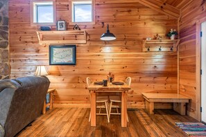 A cozy cabin interior with a wooden dining table, a sofa, and a stone wall. - Mountain views and a cozy hot tub! - Always (Gatlinburg)