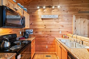 A compact kitchen with wooden walls, a stove, a microwave, and a sink.