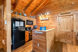 A compact kitchen with wooden walls, a black refrigerator, a microwave, and a coffee machine. - Mountain views and a cozy hot tub! - Always (Gatlinburg)