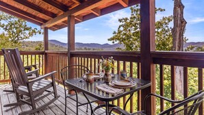 Une terrasse en bois avec une table dressée pour le repas, offrant une vue sur un paysage montagneux.