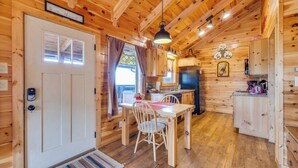 A wooden cabin interior with a dining area, kitchen, and a door with a number sign.