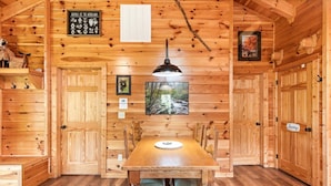 L’intérieur d’un chalet en bois comprend une table à manger, des chaises, un luminaire suspendu, un tableau encadré et un panneau indiquant les animaux que l’on peut trouver dans les forêts.