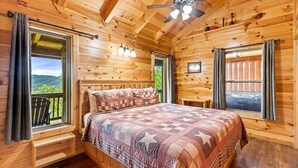 Une chambre dans une cabane en bois, avec un lit, des fenêtres et un ventilateur de plafond.