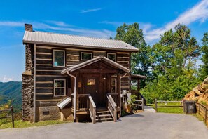 Une cabane en rondins dotée d’une véranda, de fondations en pierre et d’un toit en métal.
