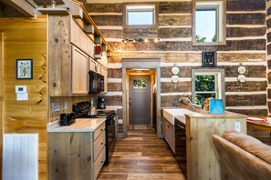 Interior de una cabaña de troncos con cocina, armarios de madera, estufa y comedor.