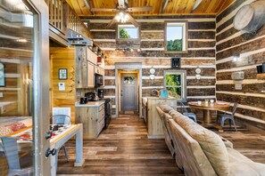 Interior de una cabaña de madera con cocina, comedor y un banco.