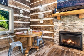 Un coin accueillant avec une table ronde en bois, deux chaises, une cheminée et un mur en pierre rustique.