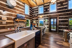 L’intérieur d’une cabane en rondins comprend une cuisine, un coin repas et une grande fenêtre.