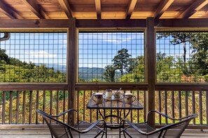 A covered outdoor seating area with a table and chairs, overlooking a mountainous landscape.