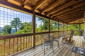 A covered outdoor area with a wooden deck, metal chairs, and a table. - Sheriff's Cabin - Mountain views from your hot tub! (Gatlinburg)