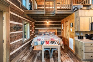 Un dormitorio rústico tipo cabaña de madera con una cama de madera, colcha de patchwork, un tablero de ajedrez y una mesita.