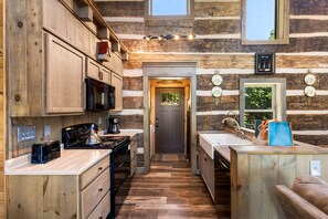 Interior de una cabaña de troncos con cocina, armarios de madera, estufa y lavabo.