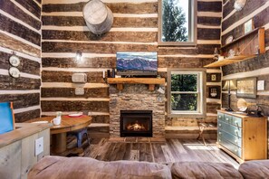 L’intérieur d’une cabane en rondins, avec une cheminée en pierre, des meubles en bois et une grande fenêtre.