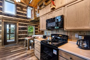 A cabin-style kitchen with a stove, microwave, and wooden cabinets.