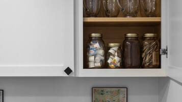 A kitchen with a white cabinet containing glassware and jars, a Cuisinart toaster, a coffee maker, and a framed botanical print.