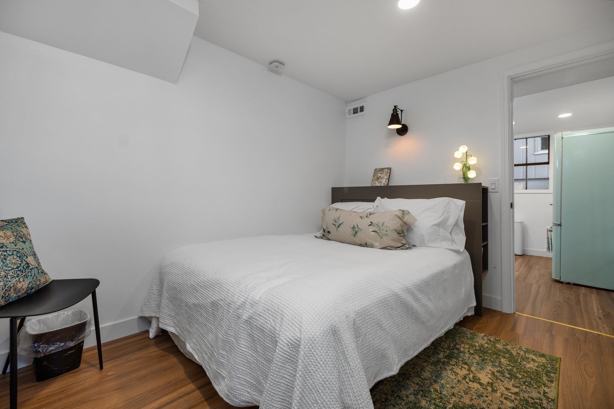 Een slaapkamer met een bed, een stoel, een prullenbak en een deur.